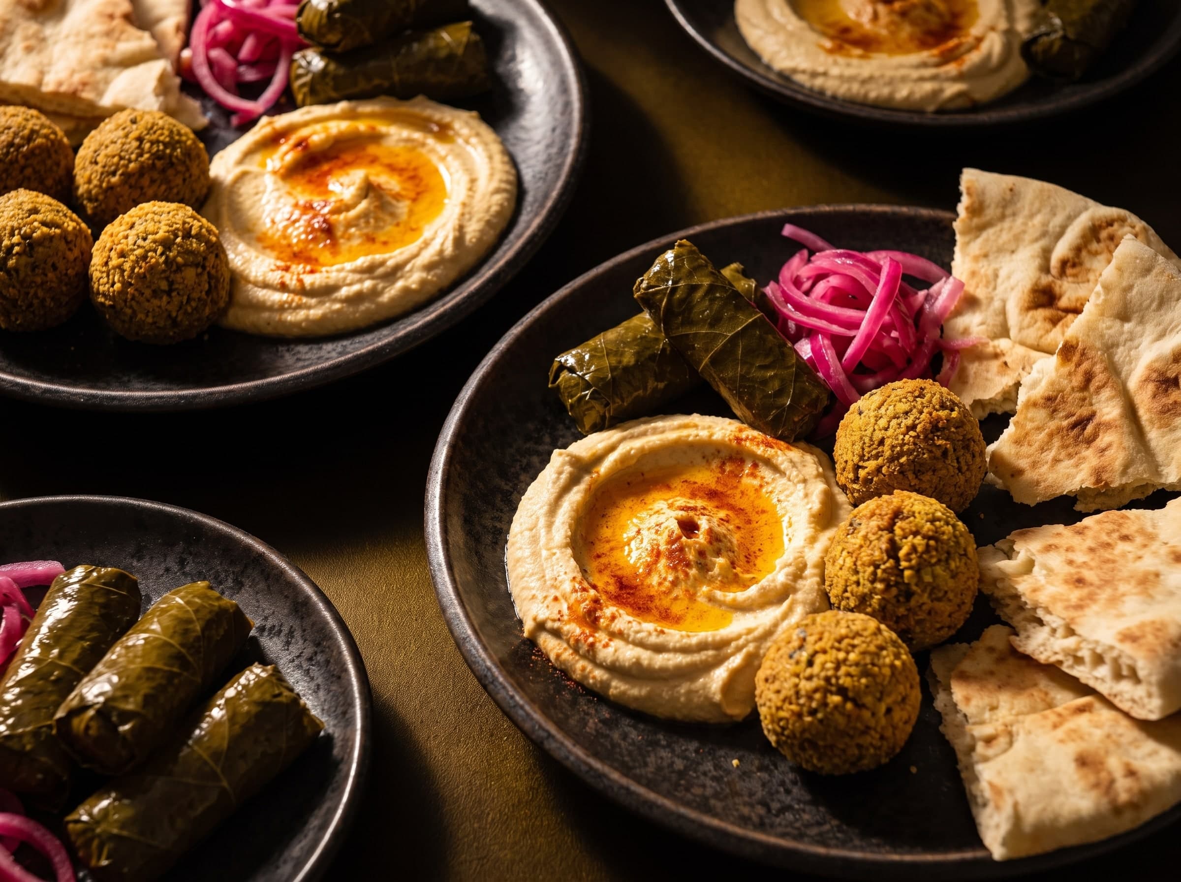 Hummus mit Paprikaöl, Falafel, gefüllte Weinblätter, eingelegte Zwiebeln und Fladenbrot auf dunklen Tellern